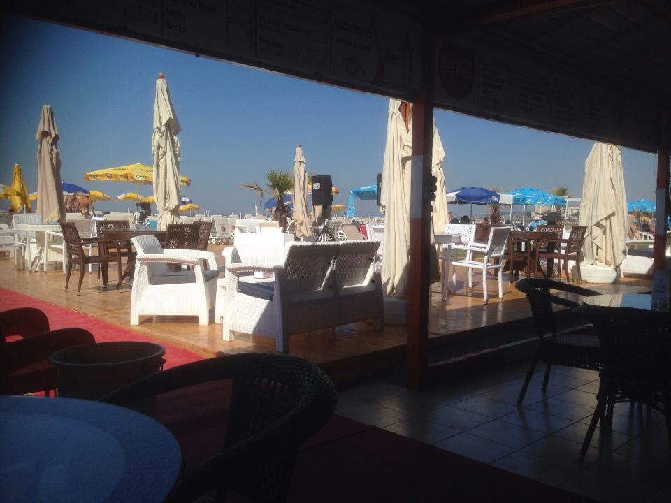 Deniz Feneri Beach barının gölgeli iç mekânından denize bakan oturma alanı ve şemsiyeler